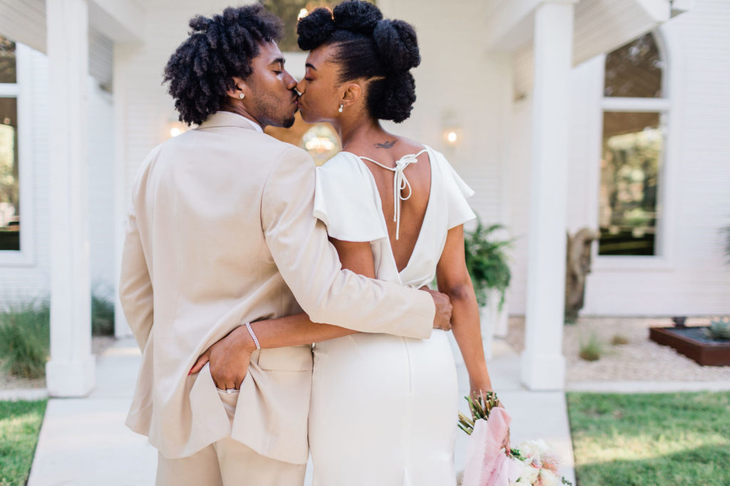 The couple standing side by side and kissing in front of the chapel.